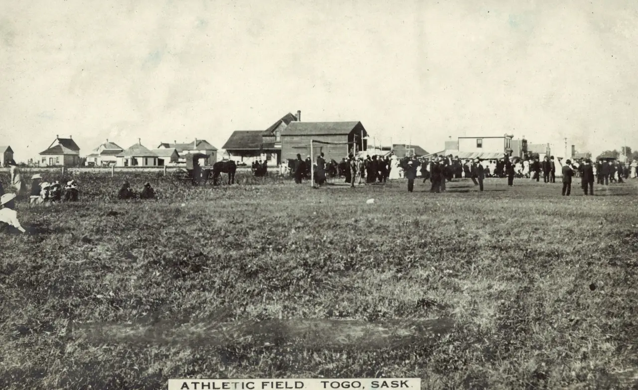 Athletic field with crowd and town buildings, about 1910